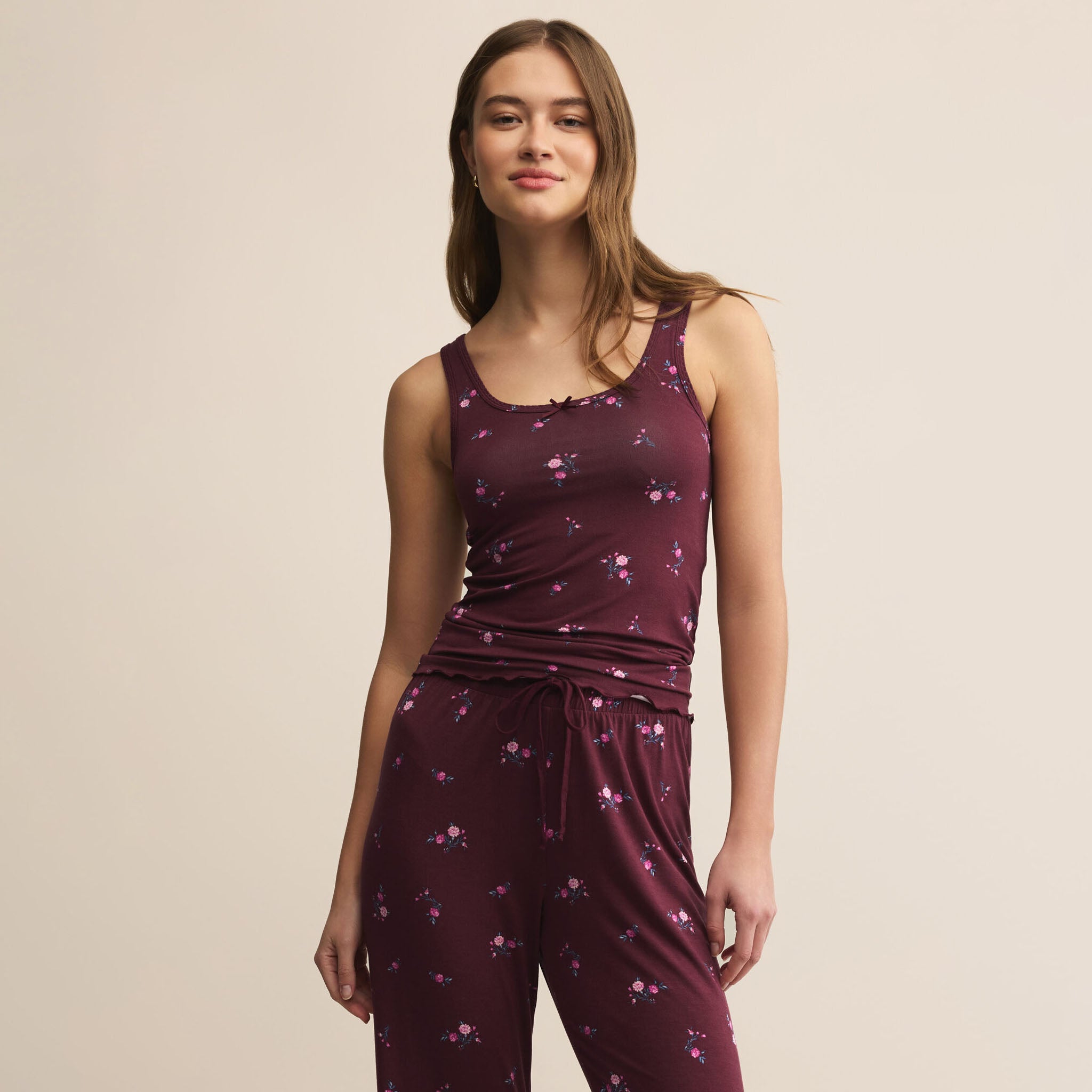 Woman wearing a maroon sleeveless top and pants with a subtle pattern on a beige background