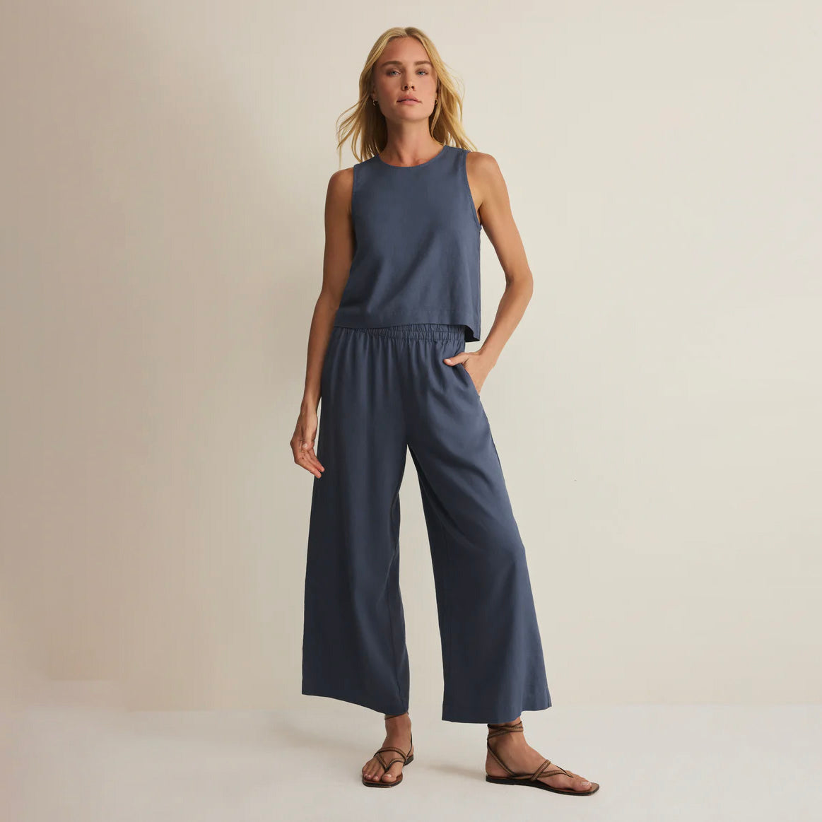Woman wearing a sleeveless navy top and wide-leg pants on a beige background