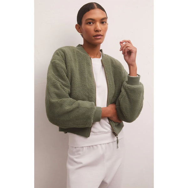 Model wearing Z Supply Take Flight Reversible Jacket in Evergreen and white pants on a grey background