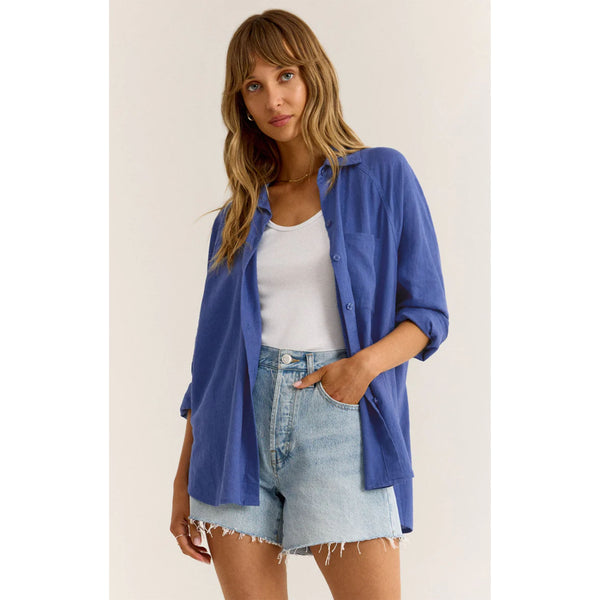 Model wearing cut off jean shorts and Z Supply The Perfect Linen Top in Blue Wave in front of a white background