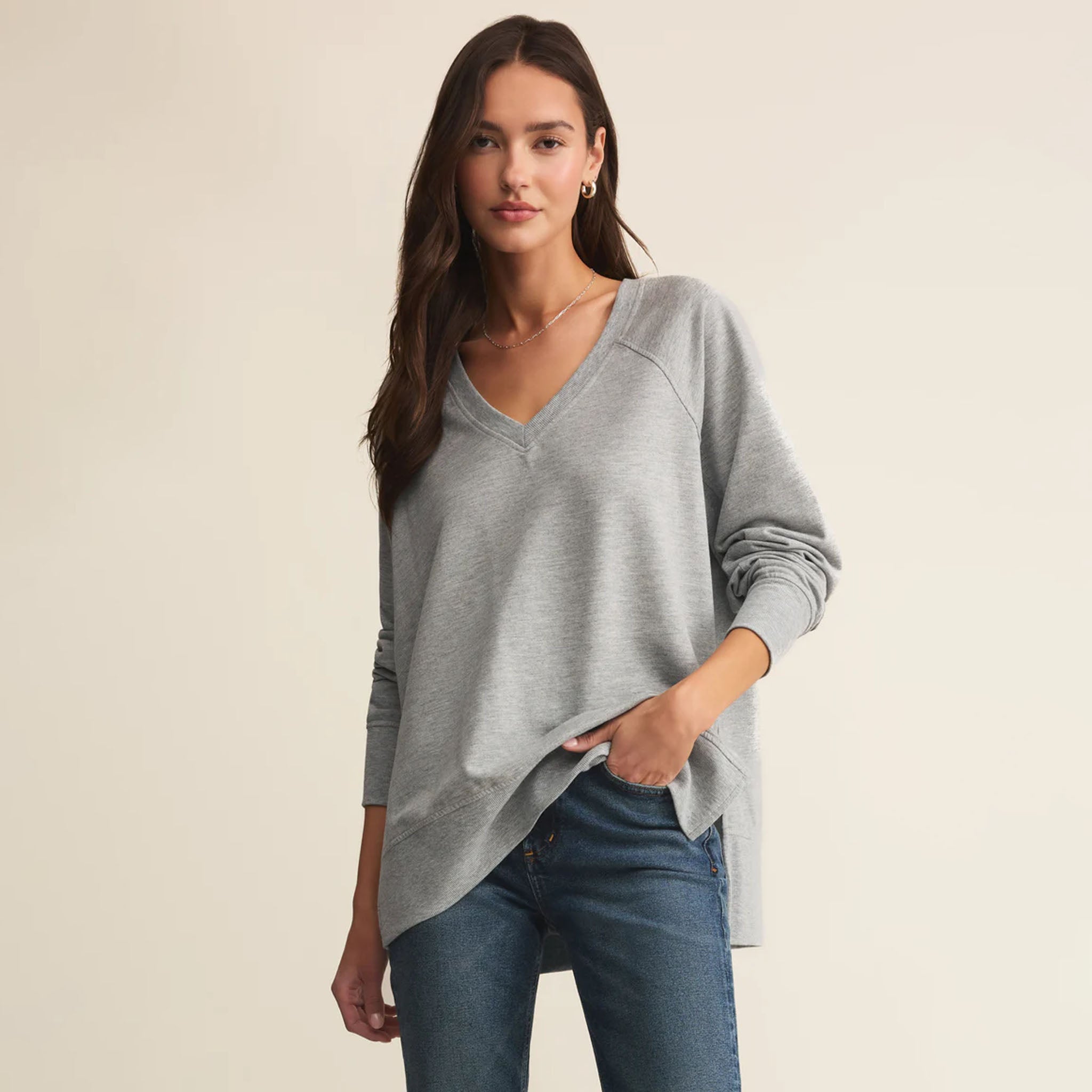 Woman wearing Z Supply Weekender V Neck in Heather Grey and blue jeans against a beige background