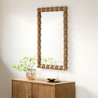 Brennan Accent Mirror in Natural on a beige wall above a table at Addison West