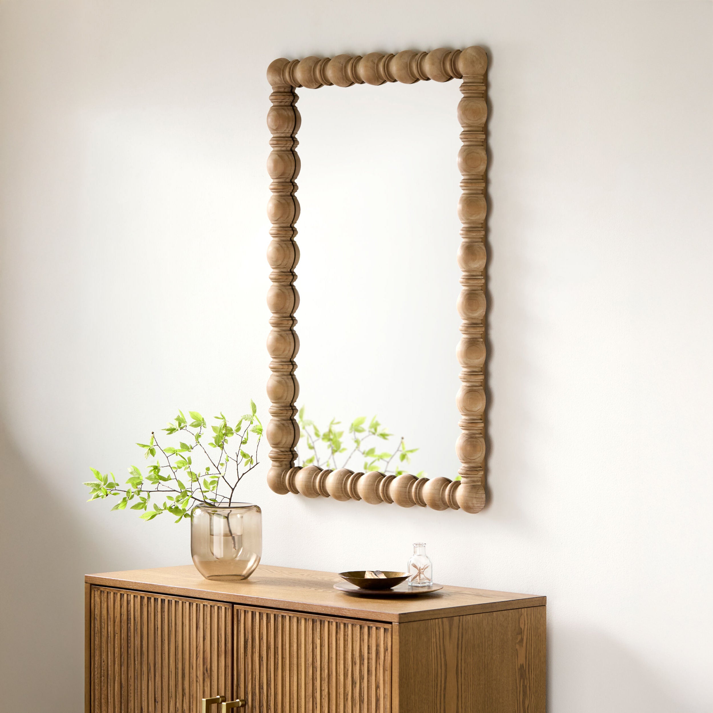 Brennan Accent Mirror in Natural on a beige wall above a table at Addison West