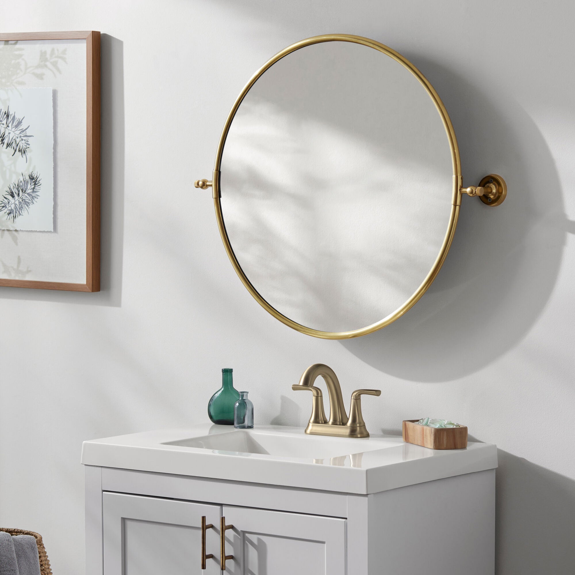 Burnish Round Accent Mirror in Antiqued Gold on a white wall in a bathroom at Addison West