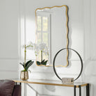 Anesley Accent Mirror in Gold on a white wall above a table at Addison West