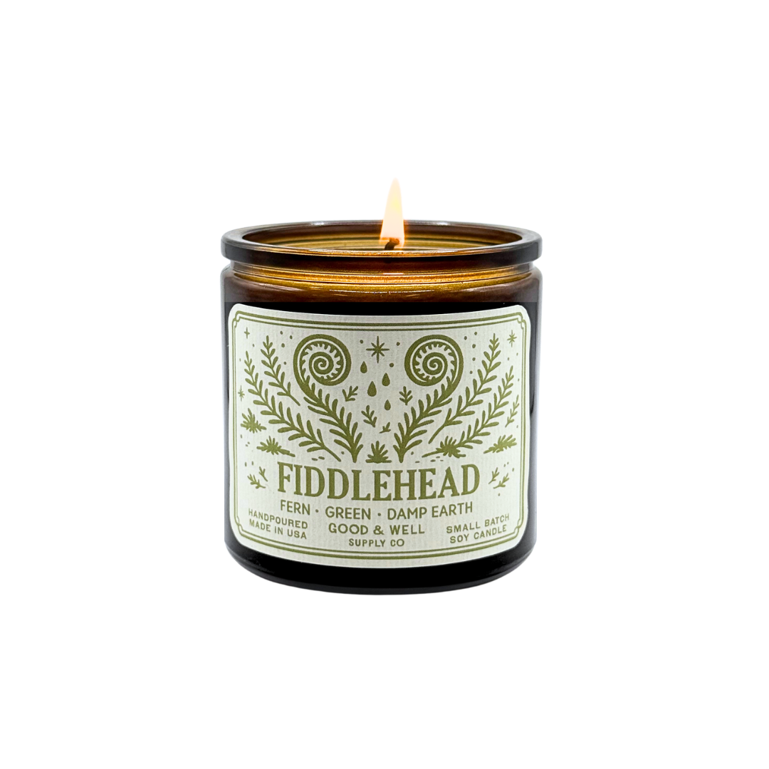 Fiddlehead candle with a lit wick on a white background