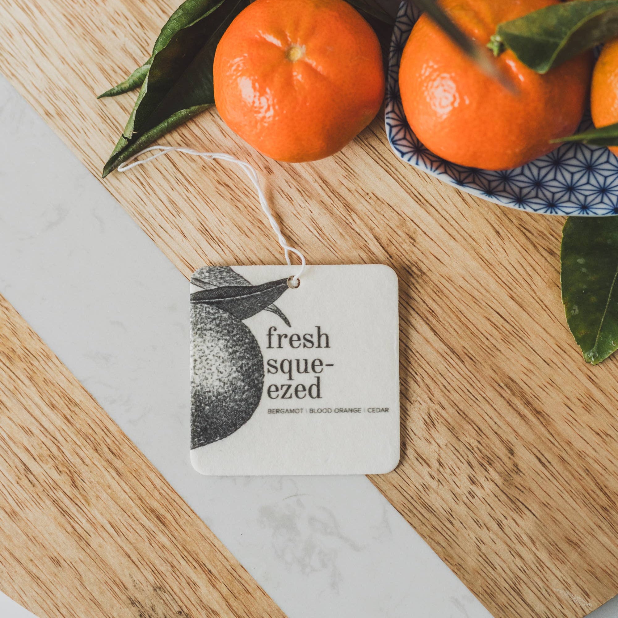 Broken top brand Fresh Squeezed Car Fresheners on a wood table next to oranges