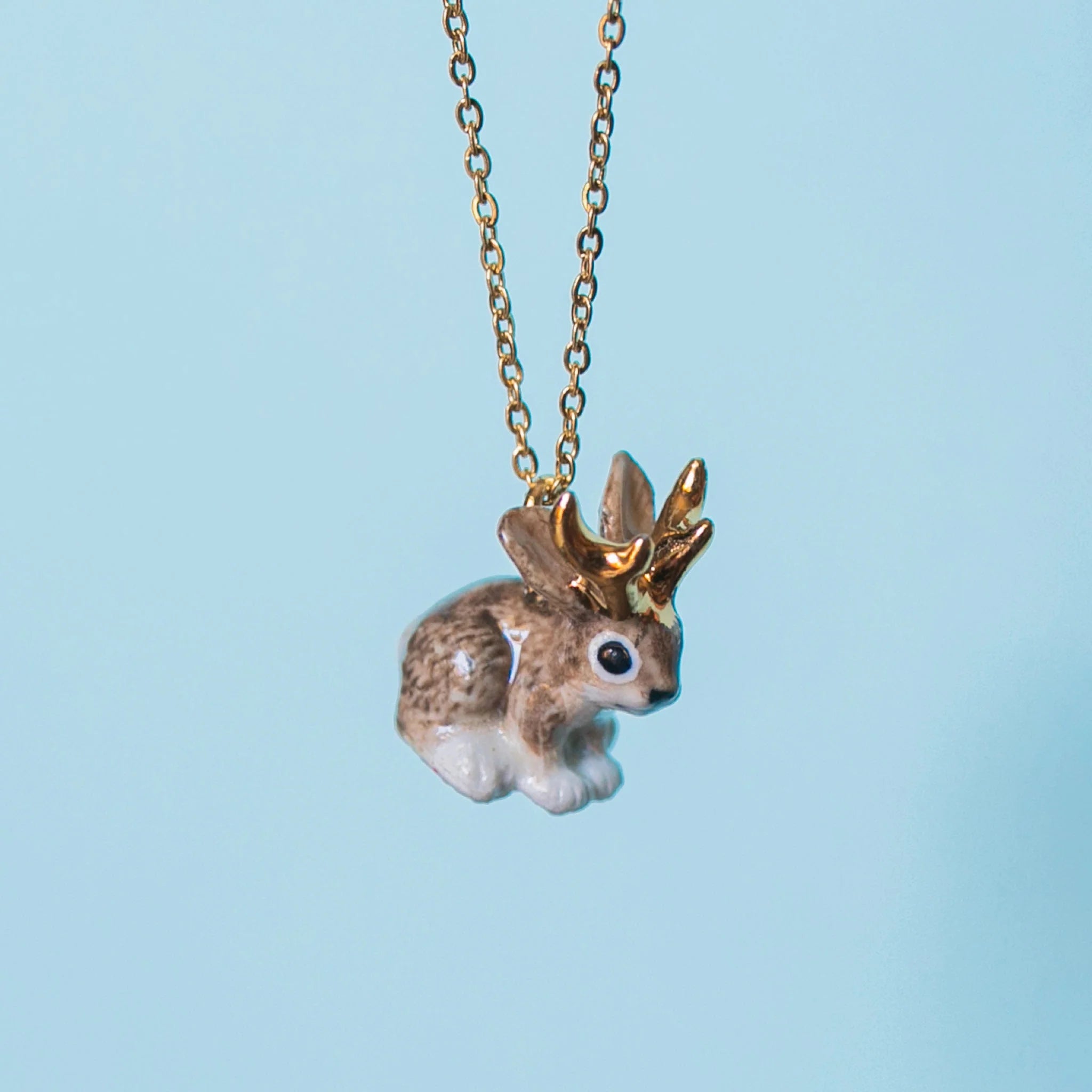 Camp Hollow Gold Jackalope Necklace on a blue background
