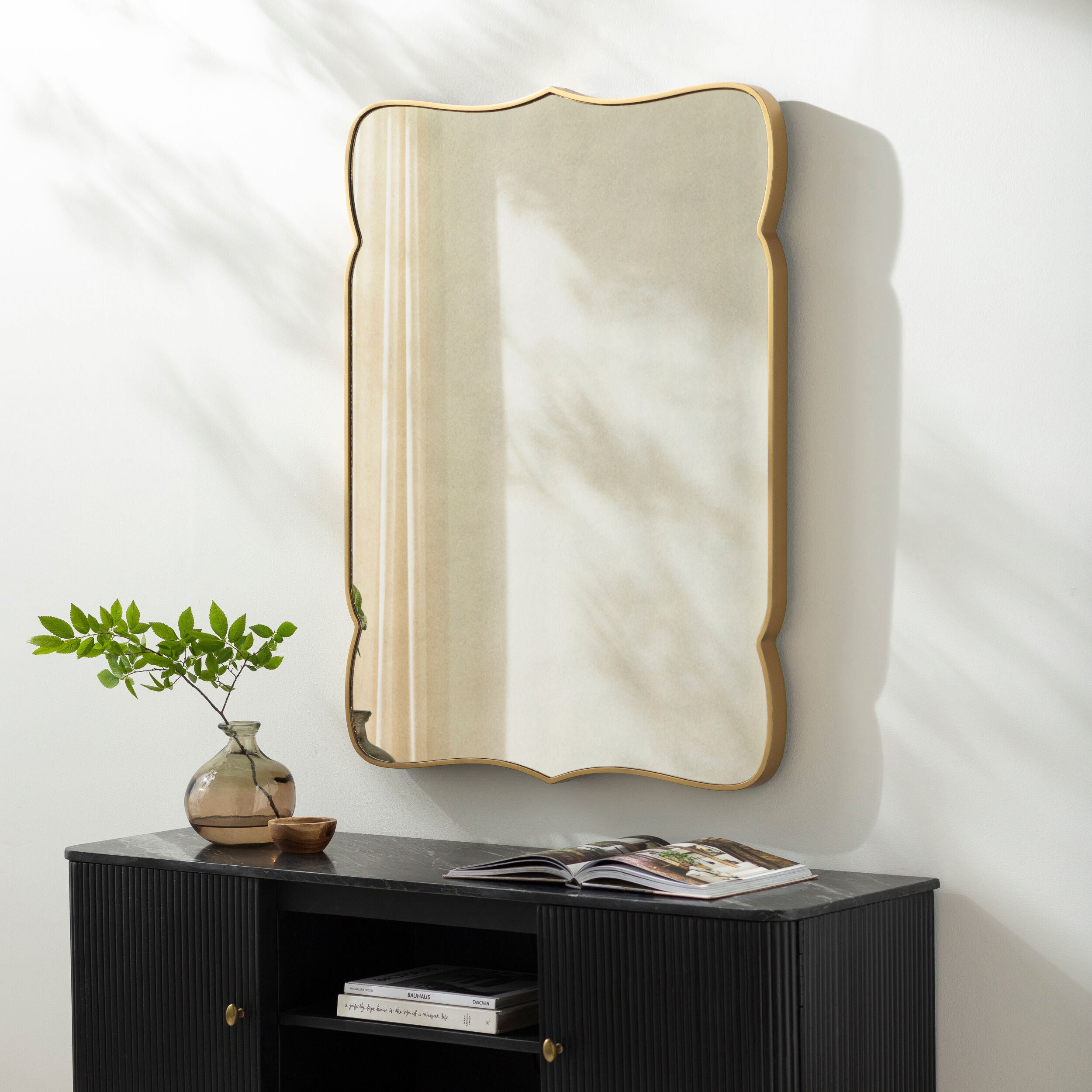 Imelda Accent Mirror on a white wall above a table at Addison West