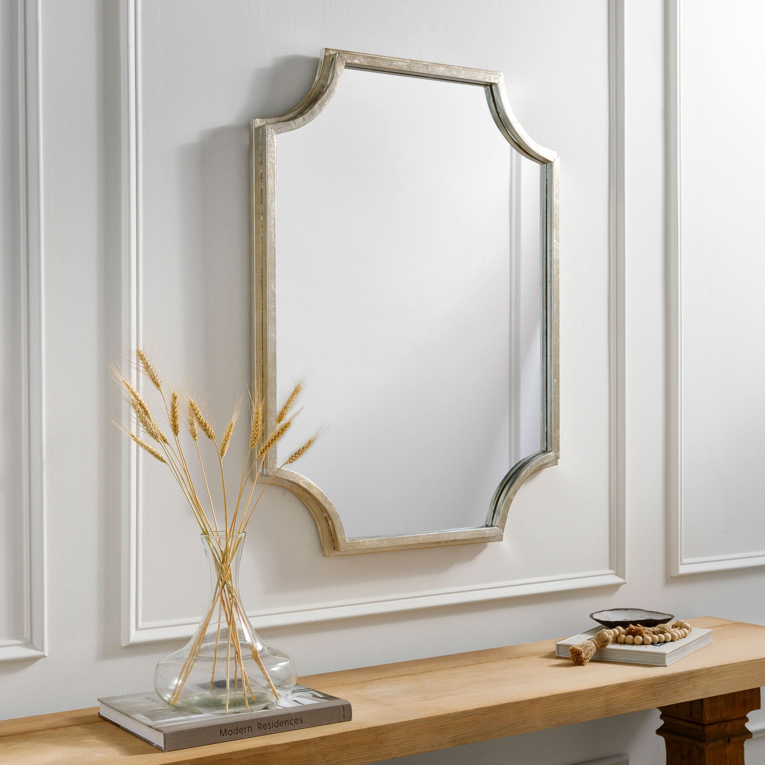 Joslyn Accent Mirror in Gilded Silver on a white wall above a table at Addison West