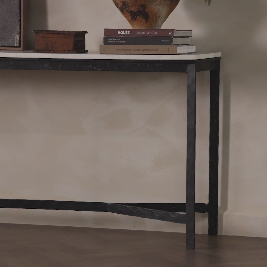 Four Hands Hammered Iron Console Table in White Marble against a white wall at Addison West