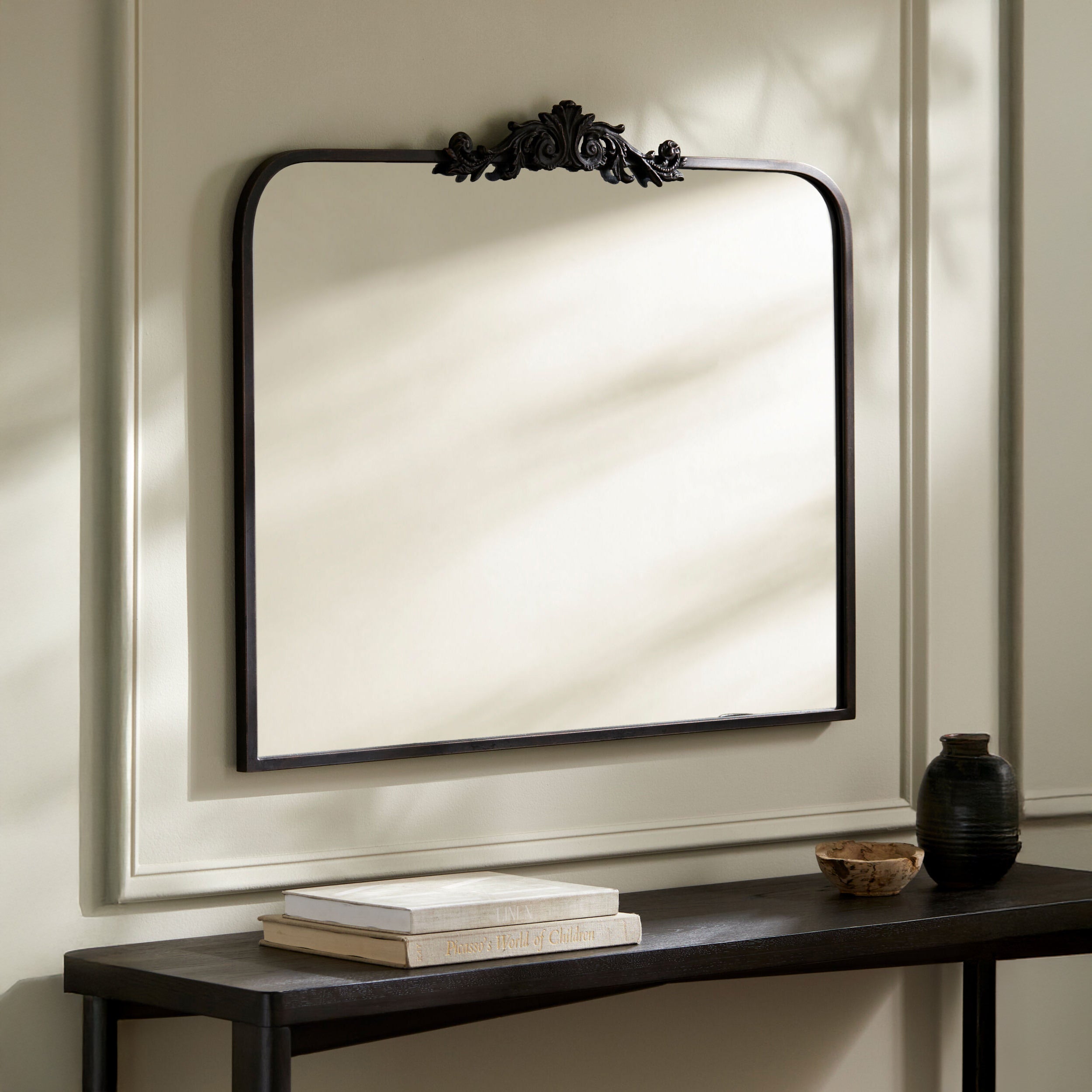 Aarlen Mantel Mirror in Antiqued Black on a beige wall above a table at Addison West