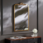 Aarlen Accent Mirror in Antiqued Gold  on a dark grey wall above a table at Addison West
