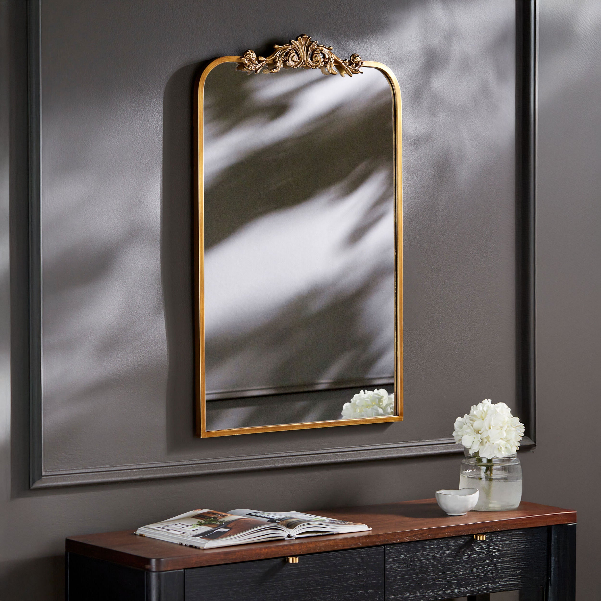 Aarlen Accent Mirror in Antiqued Gold  on a dark grey wall above a table at Addison West