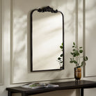 Aarlen Accent Mirror in Antiqued Black on a beige wall above a table at Addison West