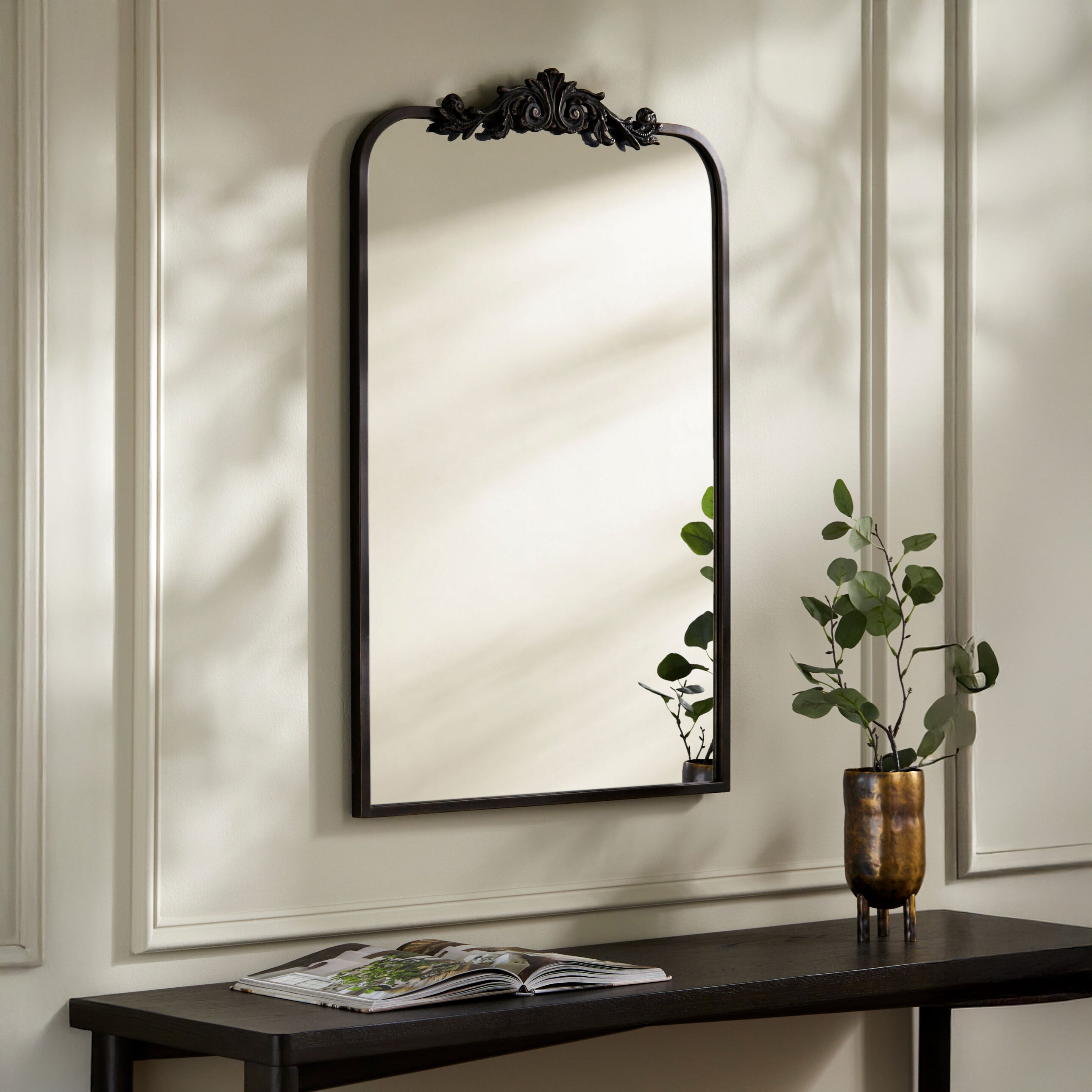 Aarlen Accent Mirror in Antiqued Black on a beige wall above a table at Addison West
