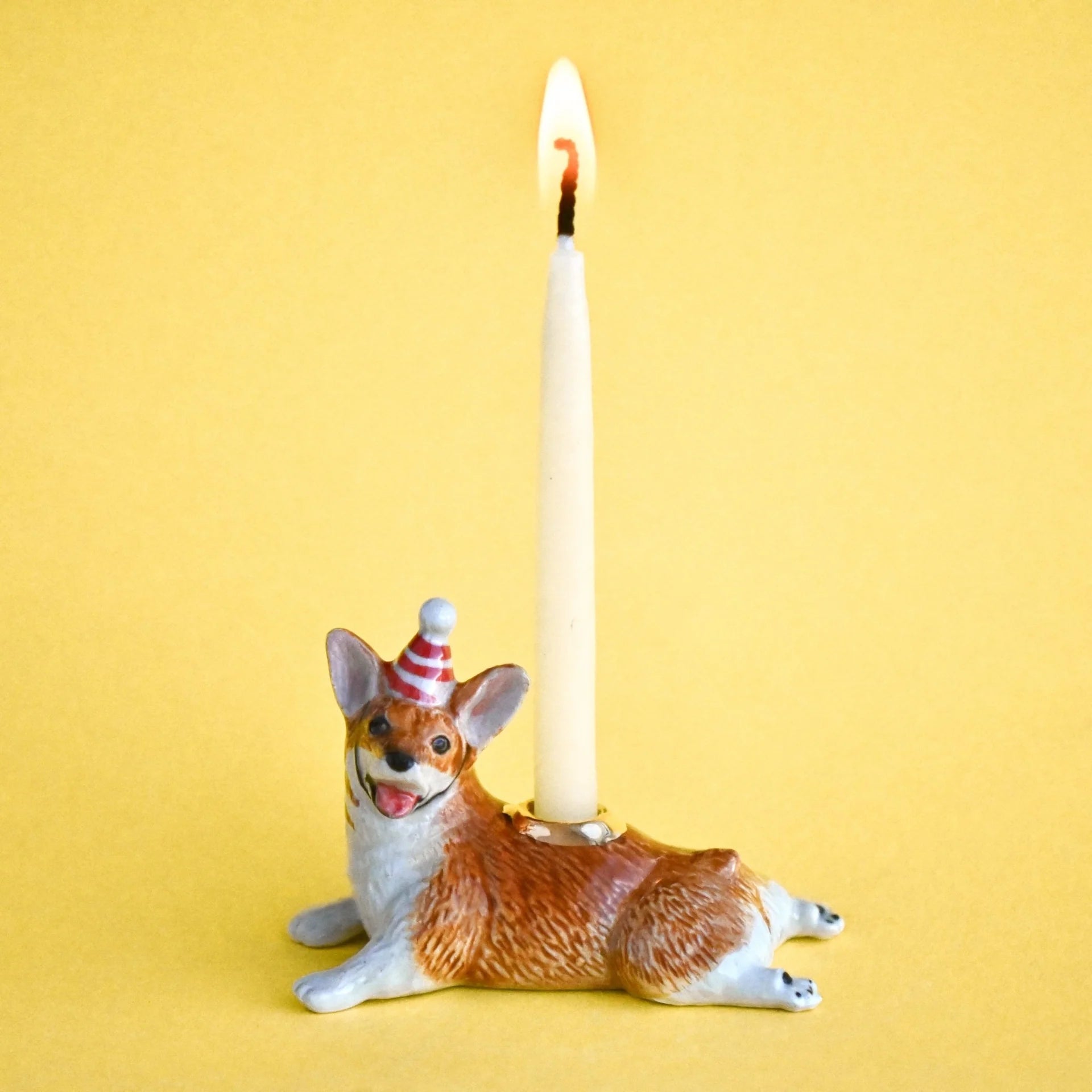Dog-shaped candle holder with a lit candle on a yellow background