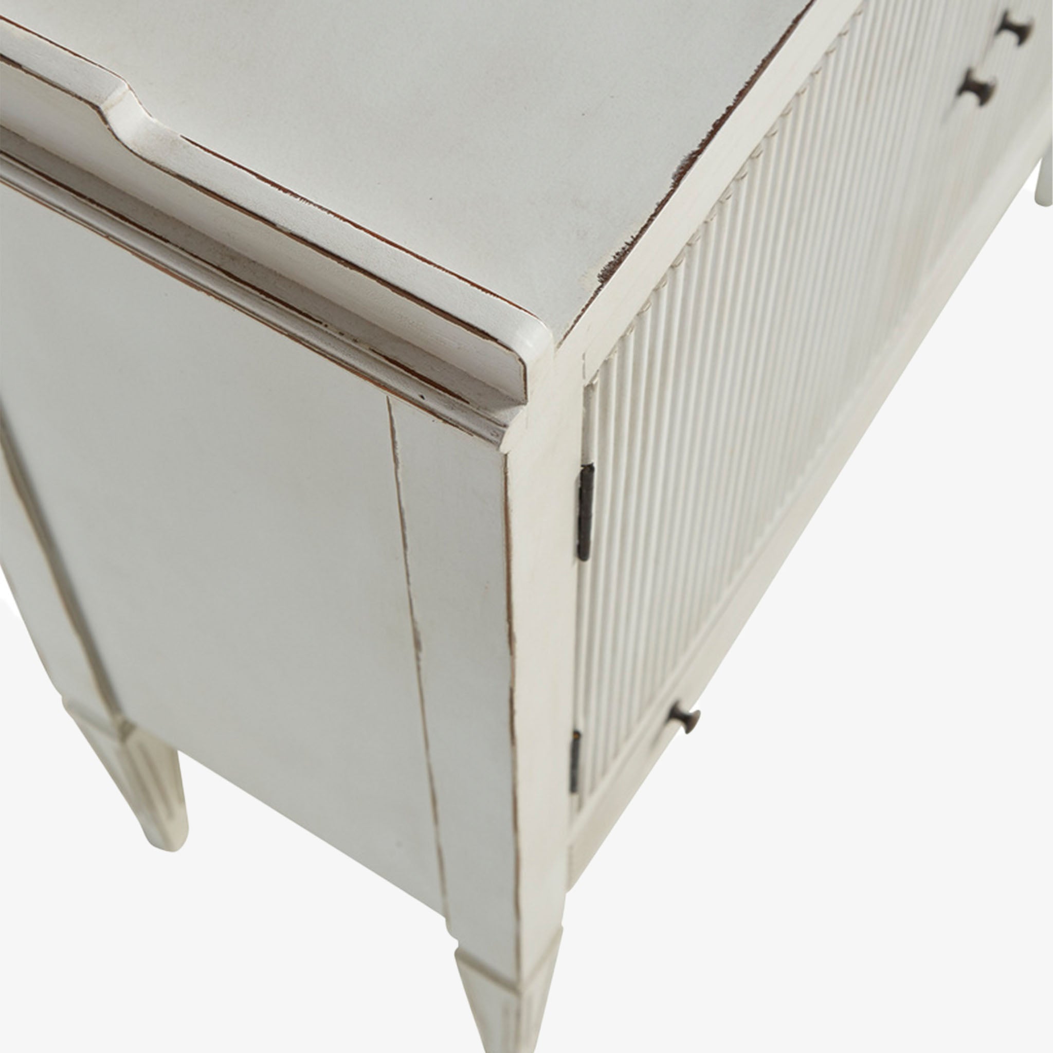 Whitewashed small console cabinet with reeded doors and tapered feet on a white background