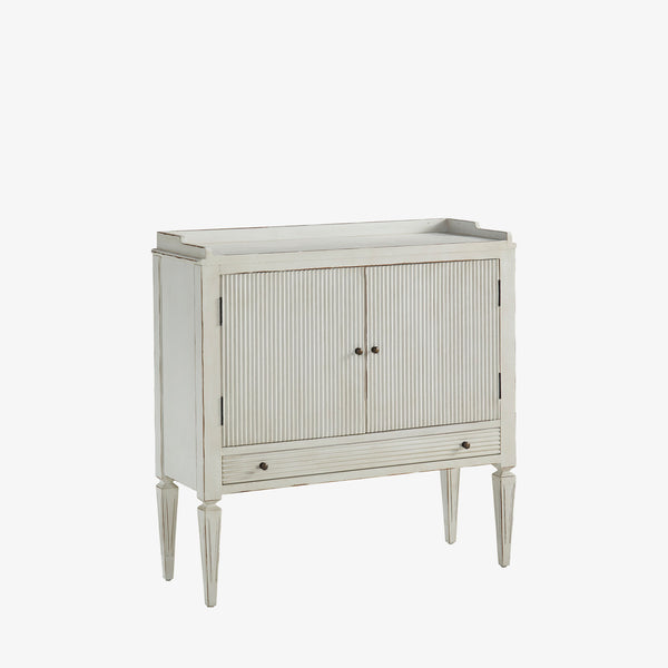 Whitewashed small console cabinet with reeded doors and tapered feet on a white background