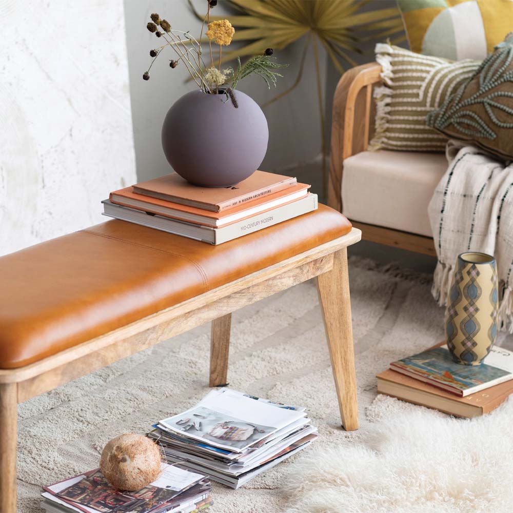 Wood bench with leather seat cushion in living room space with books and accessories