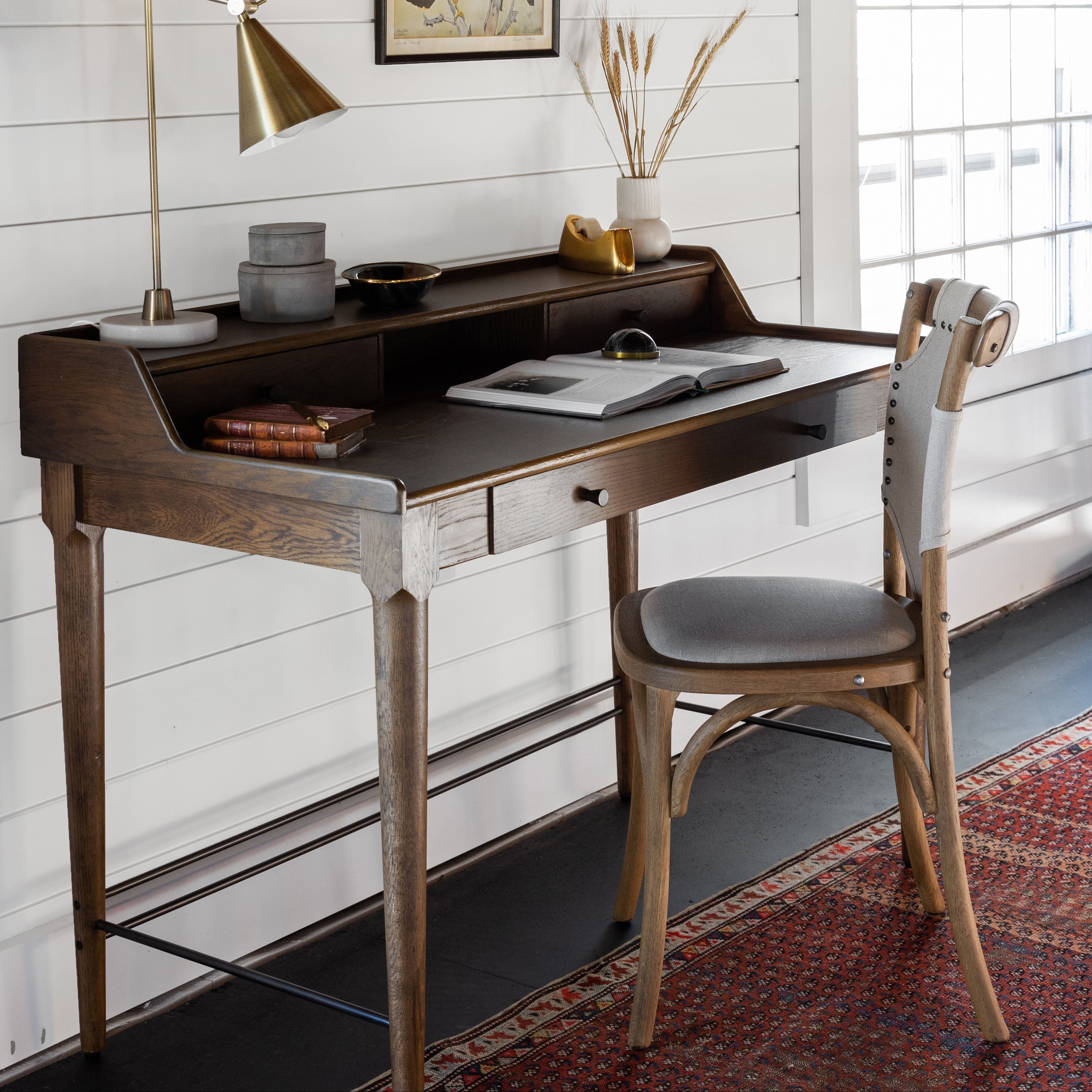Wood desk in room with beams and shiplap siding and bistro chair with wrapped canvas on red antique rug