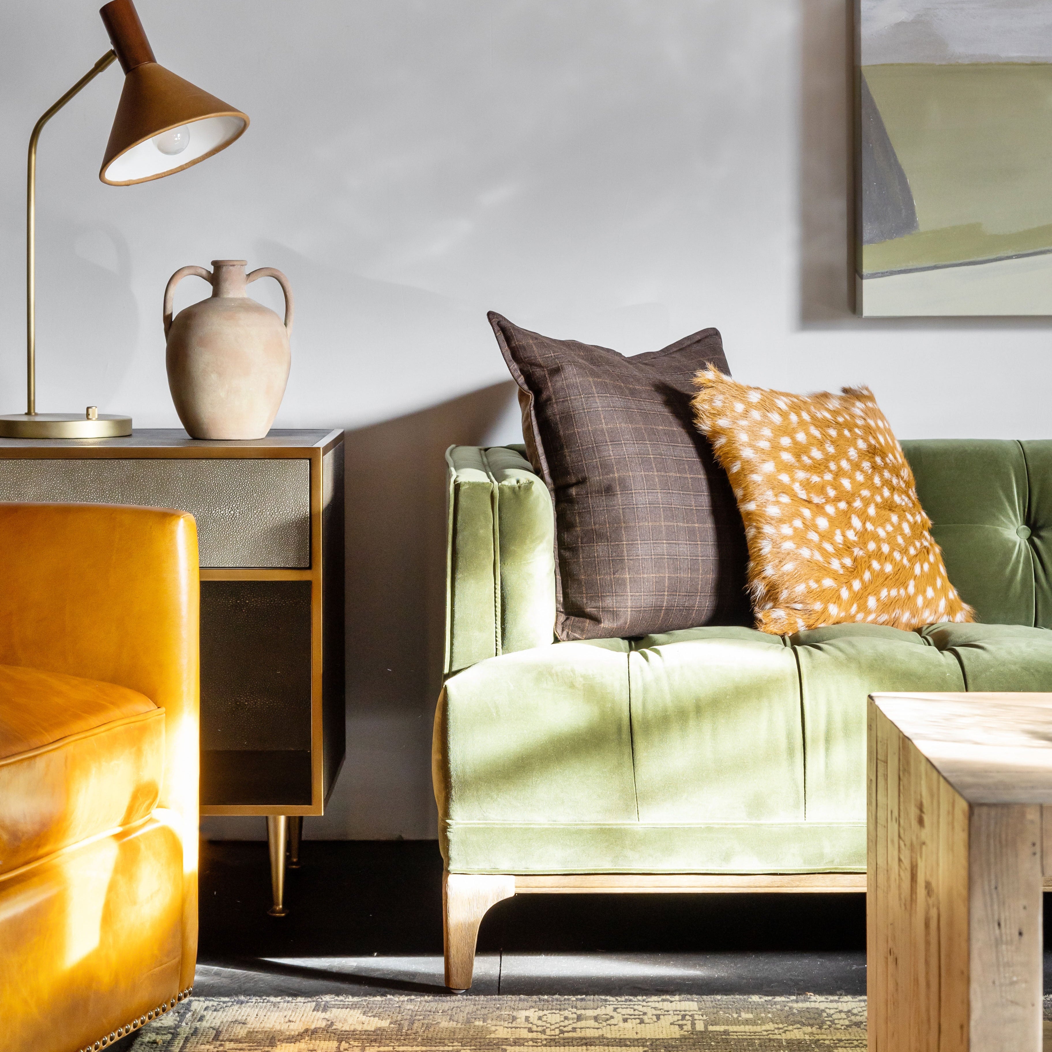 Living room area with Four hands brand green velvet Dylan sofa with paintingw with wood coffee table in front and leather armchair