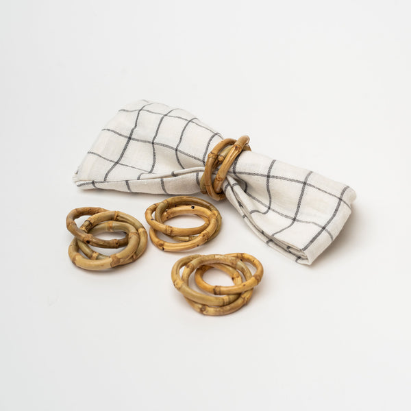 Bamboo napkin rings with three interlocking rinds on a linen napkin on a white background