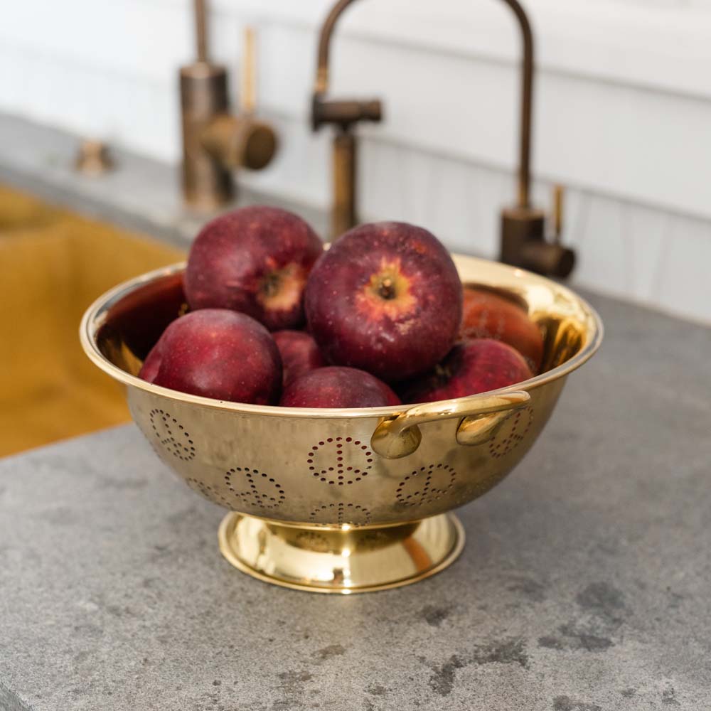 Sir Madam Brass colander with peace sign pattern perforations with apples inside on a kitchen counter