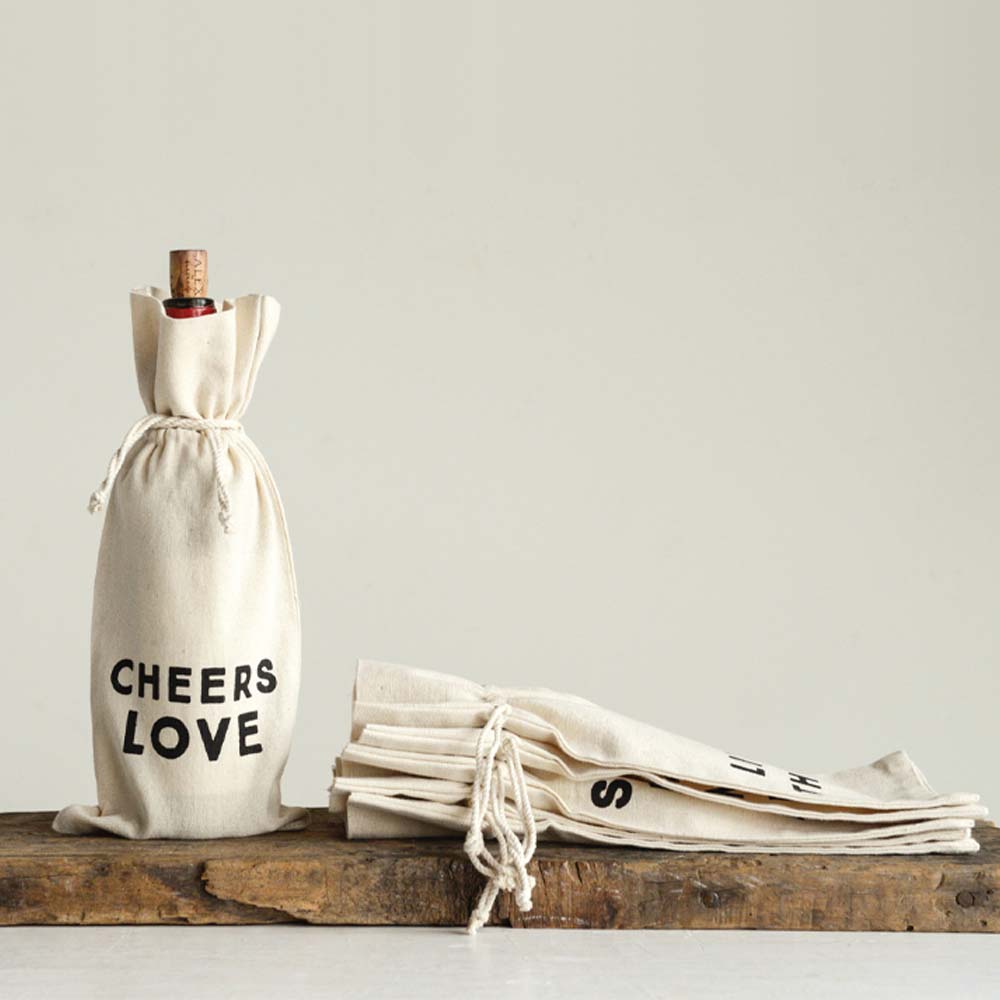 White cotton wine bag that says 'Cheers love' with a bottle inside on a wood shelf
