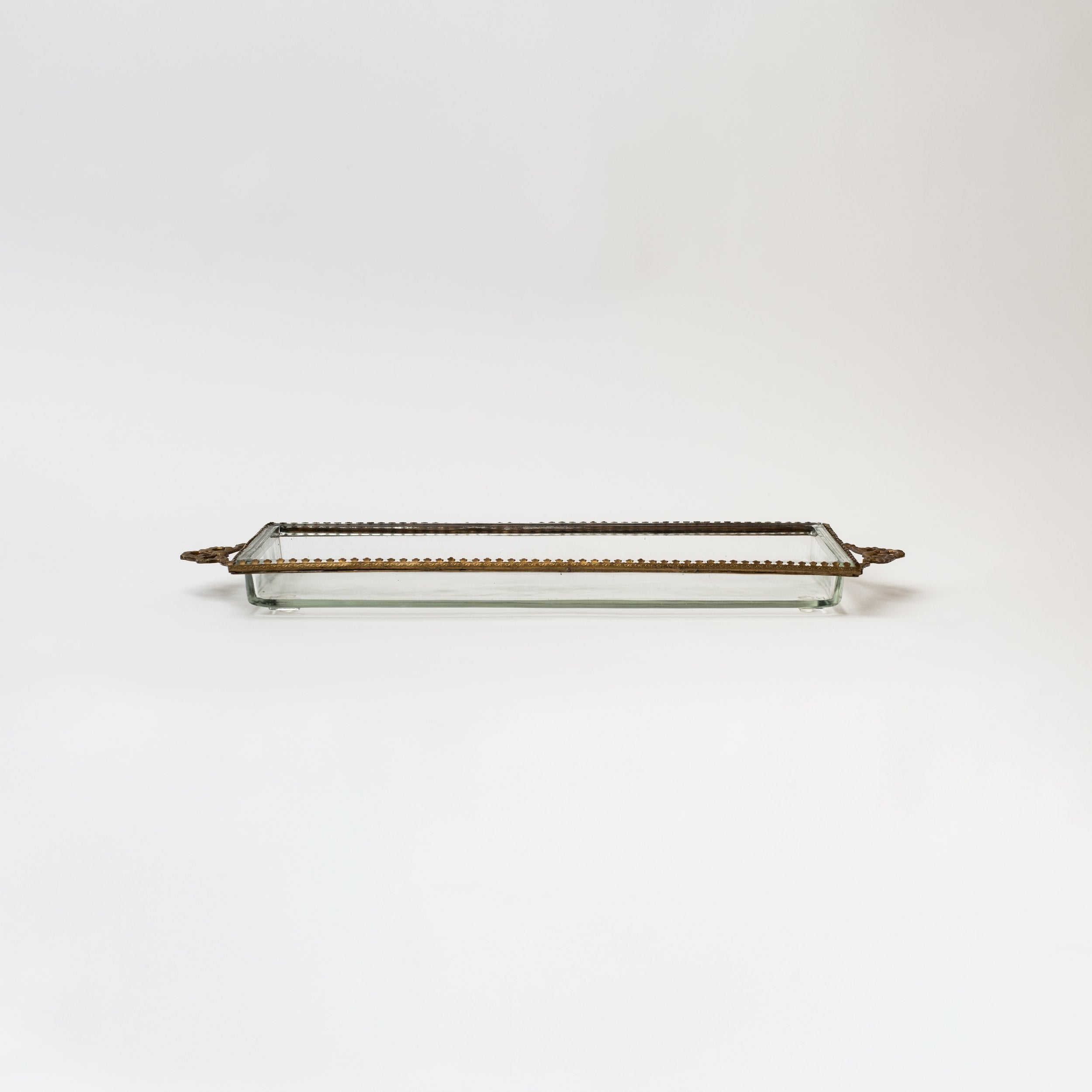Glass tray with metal brass scallop edging and decorative metal bows on ends on a white background