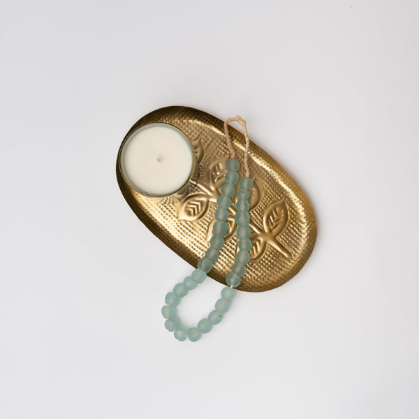 Brass tray with candle and aqua glass decorative beads on a white background