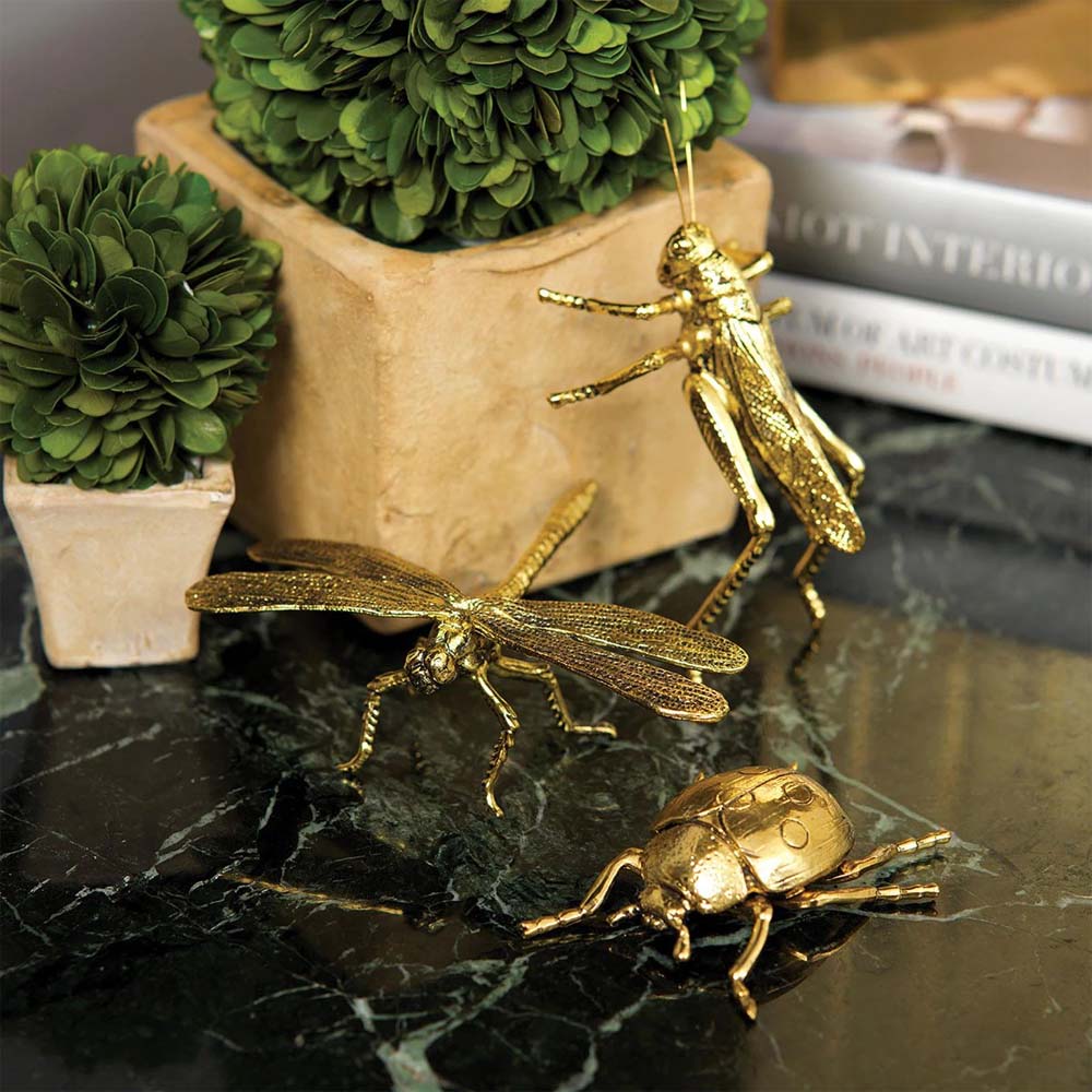 Collection of gold finish small dragon fly, grass hopper and lady bug sculptures together on a table with books
