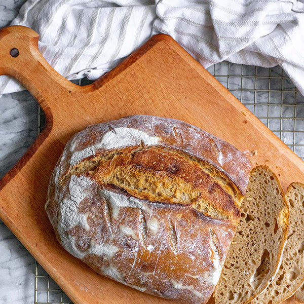 JK Adams maple paddle serving board on a counter with a cooling rack and load of bread