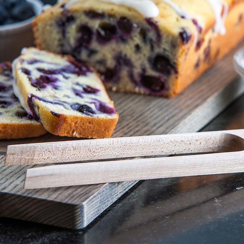 Toast tongs with blueberry bread on a wood board