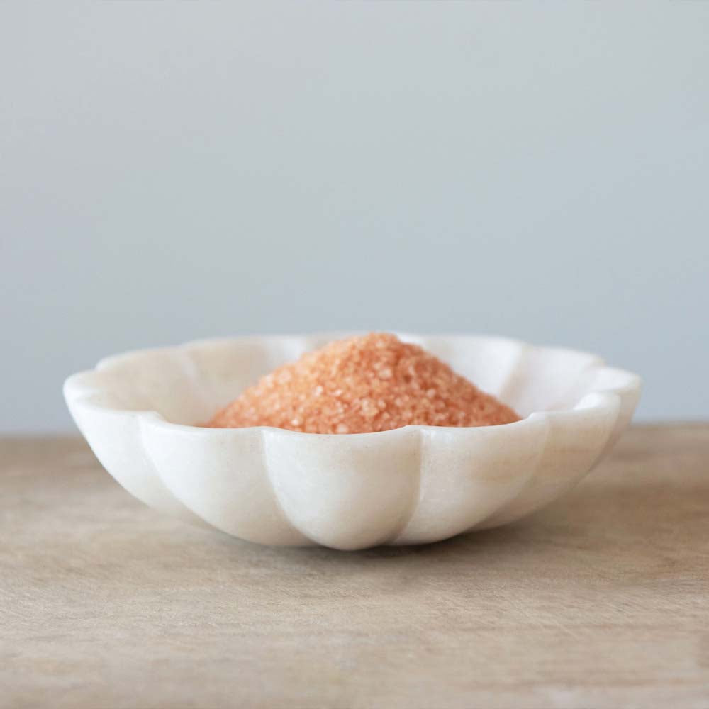 Marble dish shaped like a flower filled with pink Himalayan sea salt on a brown counter