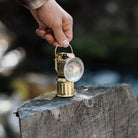 Hand holding barebones brand brass miner's lantern on a log
