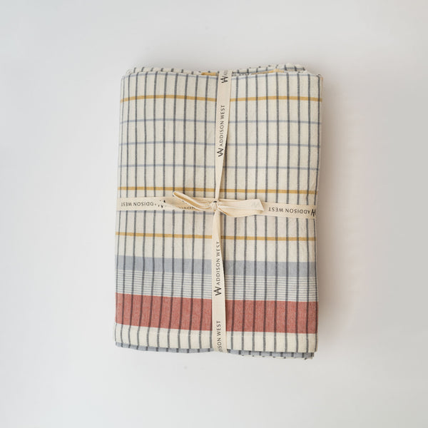 Off white tablecloth with blue, yellow and red plaid pattern tied with ribbon on a white background