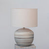 Stoneware lamp with muted stripes in browns and blues and linen shade on a grey background