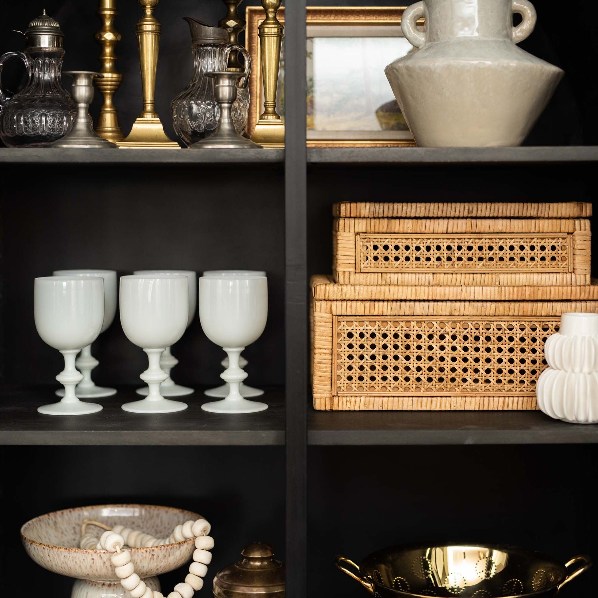 Two cane and rattan boxes by creative coop with glass lids in a black cabinet with other decorative items