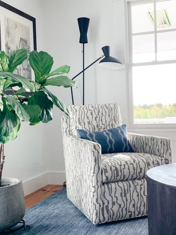 White and black swivel chair next to window with blue rug and pillow and modern black lamp. 