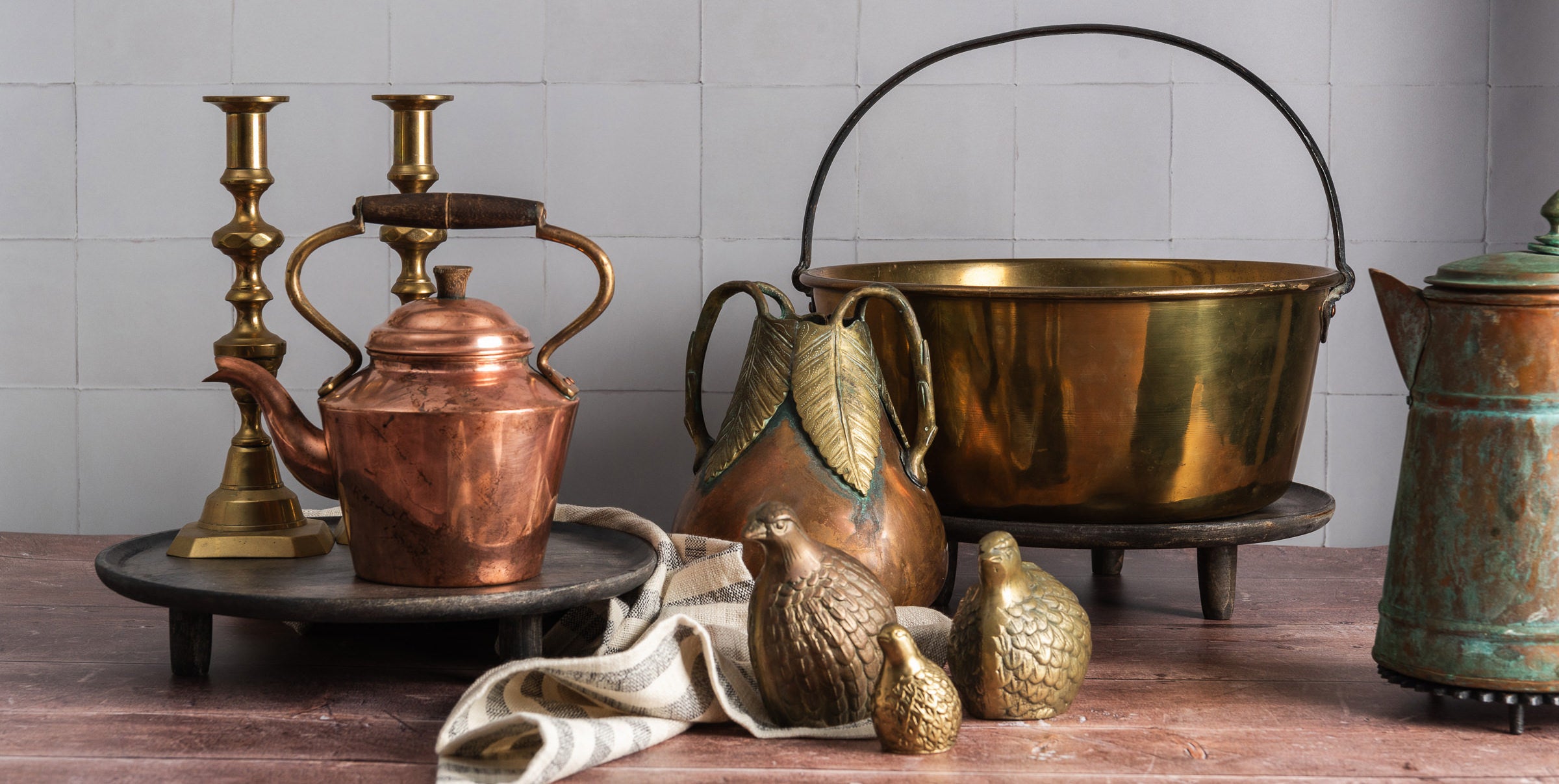vintage copper tea kettle, decor, and kitchen home goods on a wood table against a white tile background
