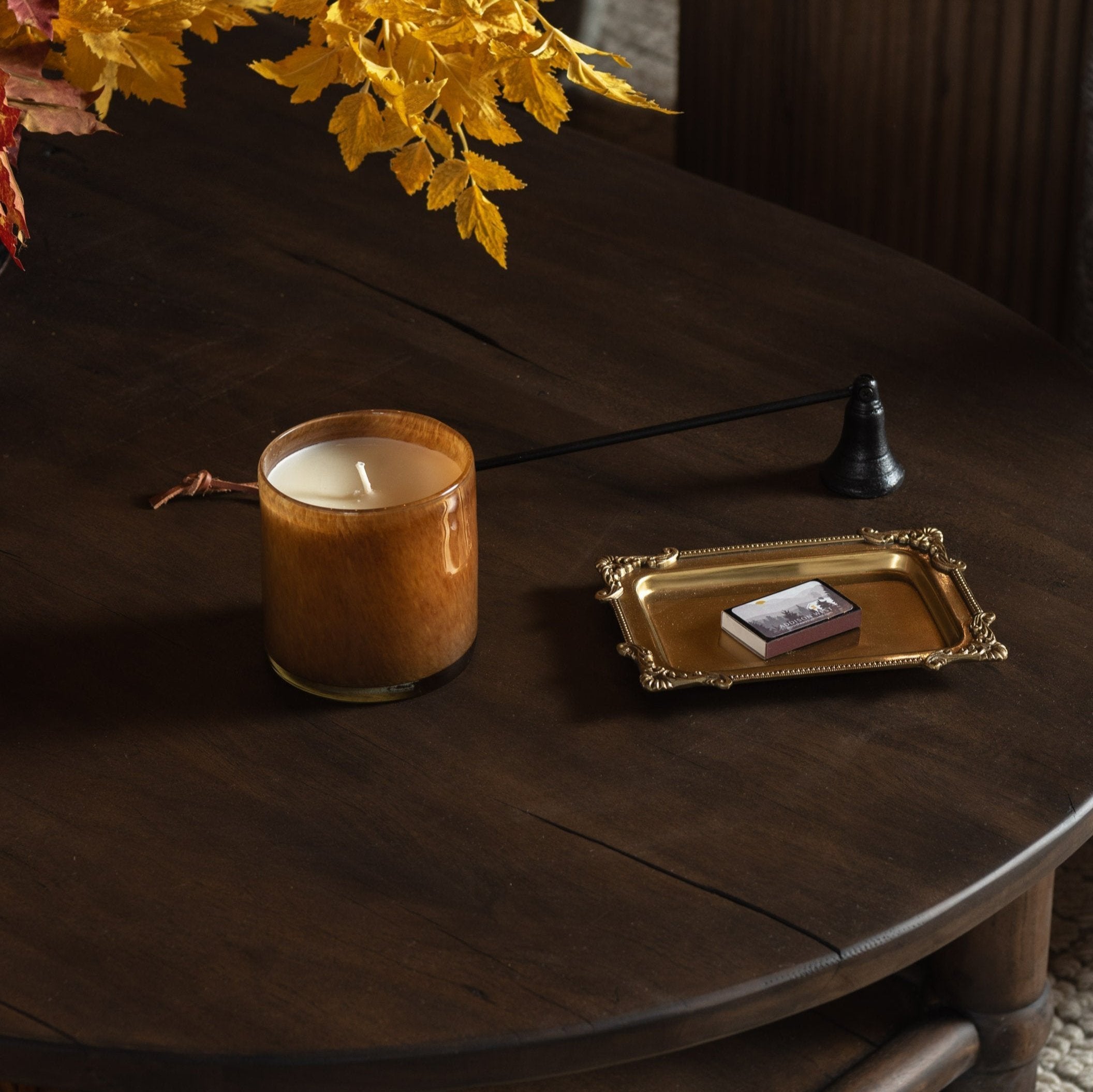 Hand blown glass candle on a dark wood table with accessories at Addison West