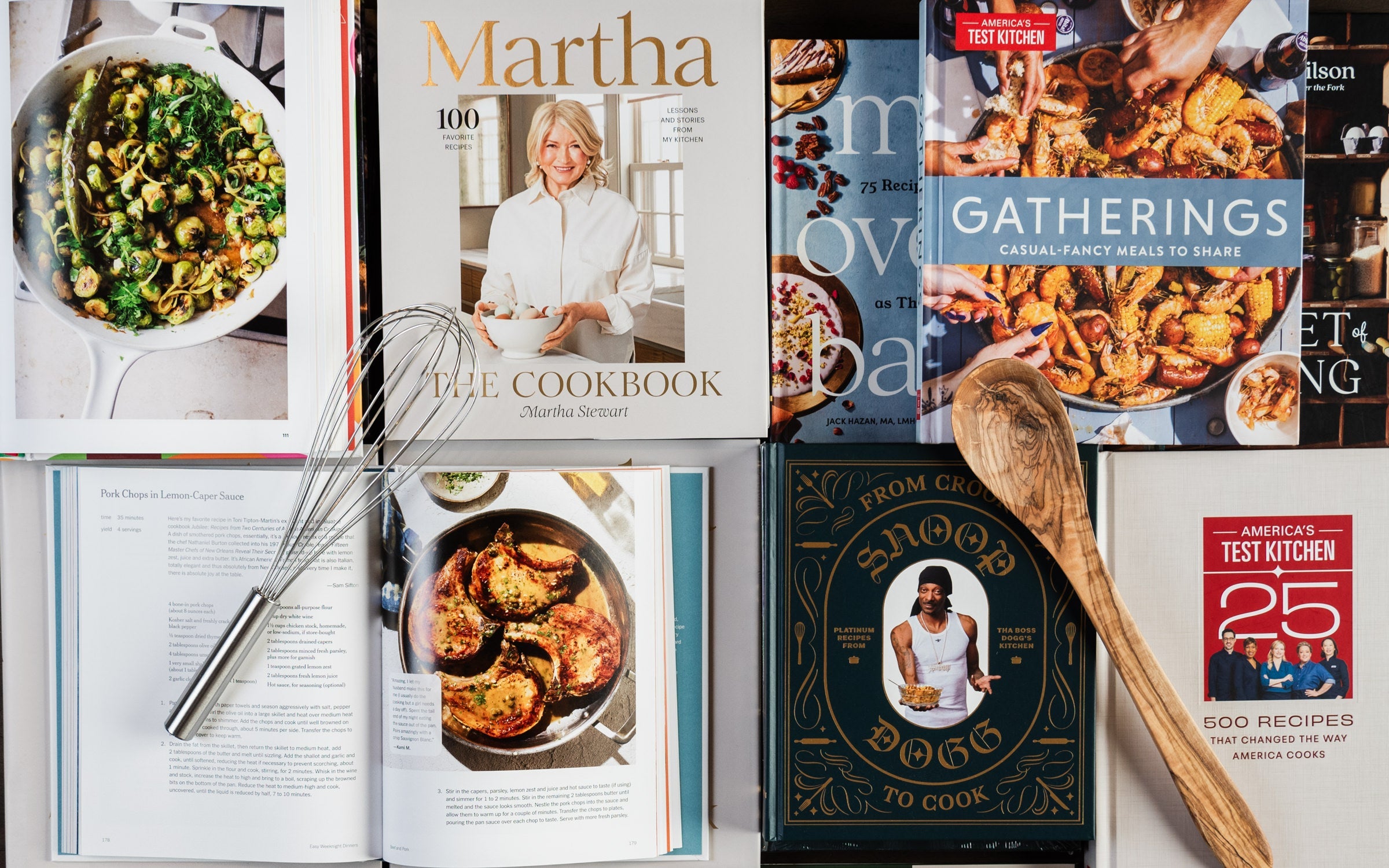 Collection of cookbooks on a table from above including Martha Stewart Cookbook, Snoop Dogg cookbook, Gatherings, Test Kitchen, and others at Addison West