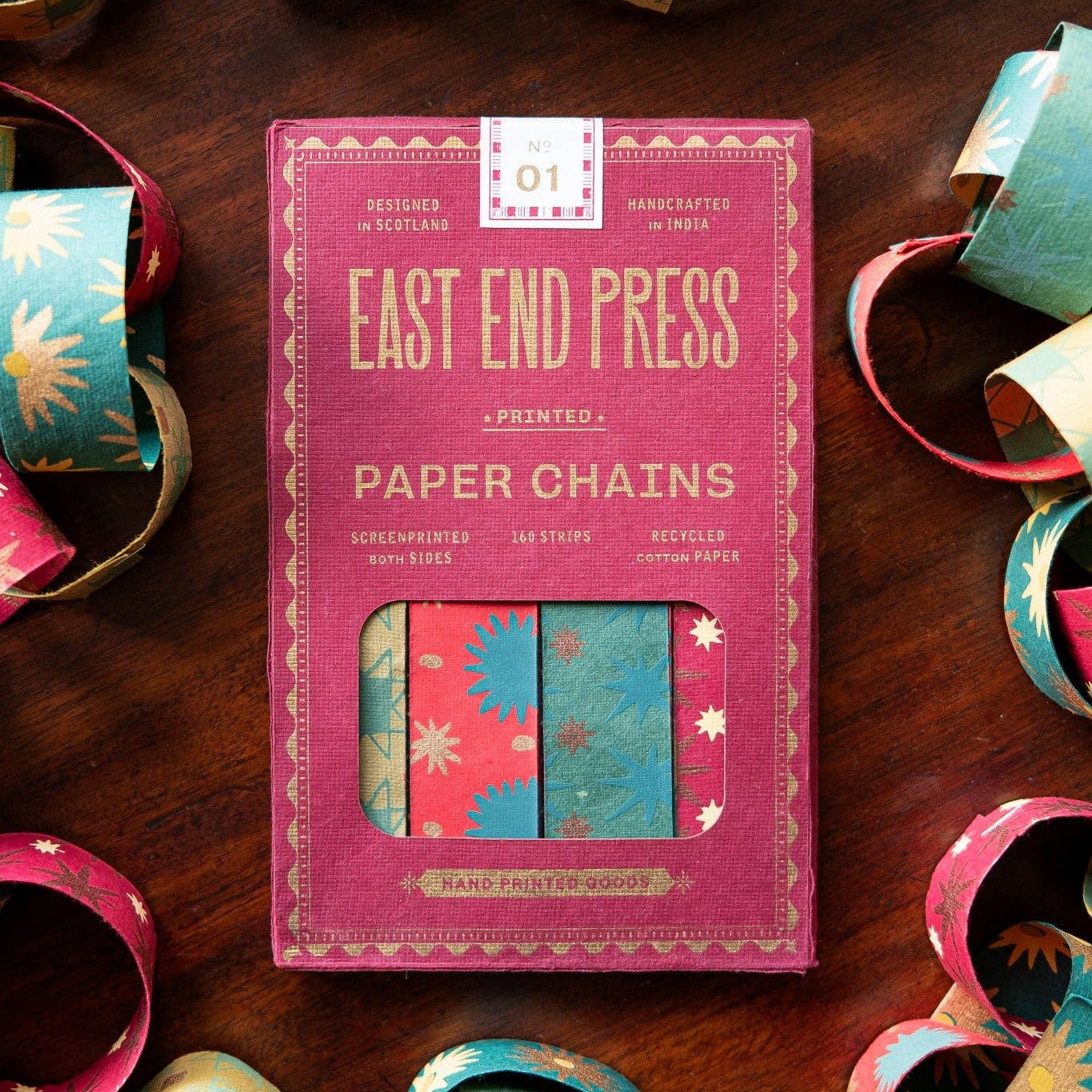 Pack of East End Press paper chains on a wooden surface with colorful paper chains around.