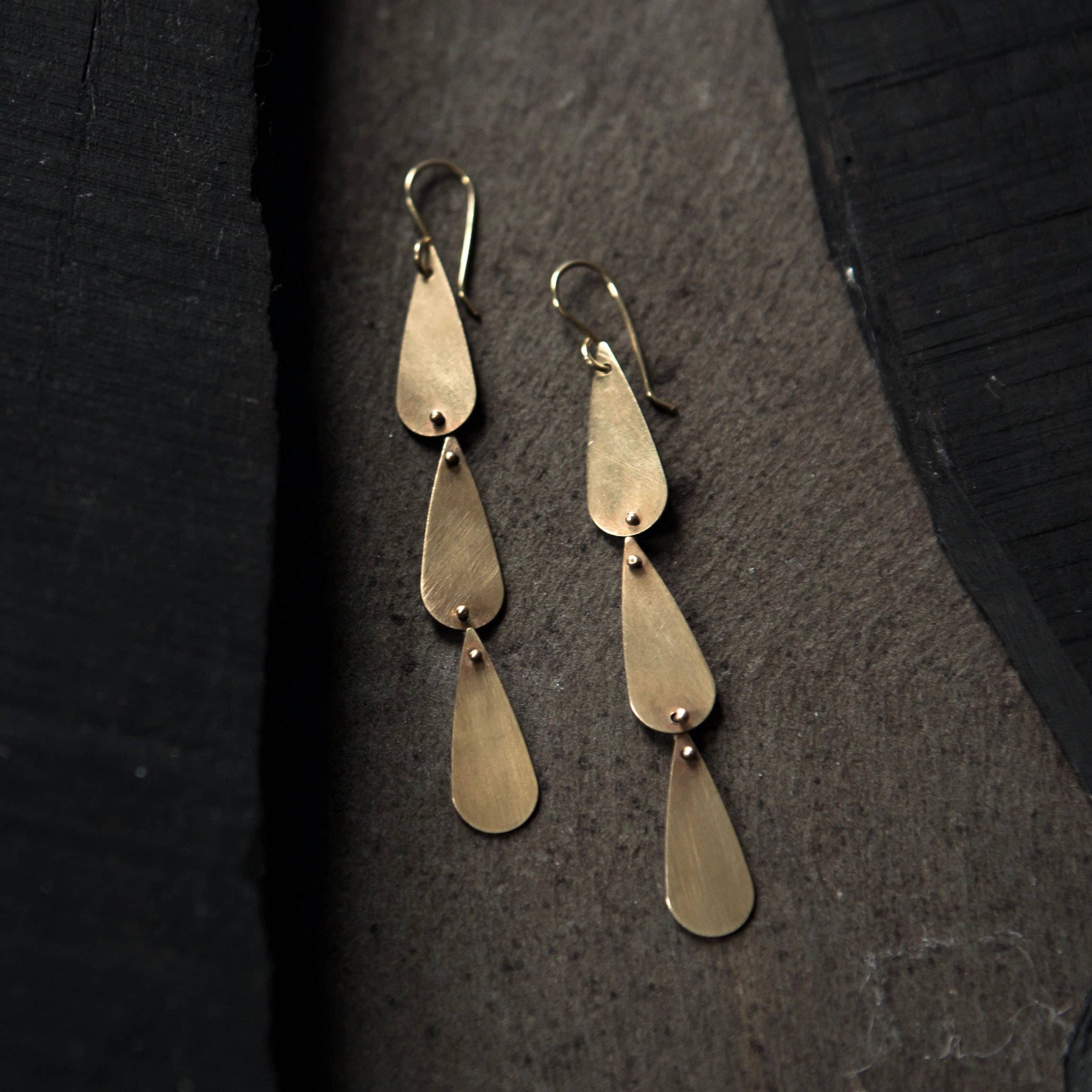 Tiny Anvil Brass Rain Earrings on a grey background at Addison West