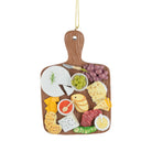A wooden charcuterie board ornament hanging ornament with a gold hanging string, featuring illustrated food items like cheese, grapes, crackers, salami, and dips on a white background.