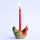 Ceramic rooster-shaped candle holder with a red candle on a light blue background