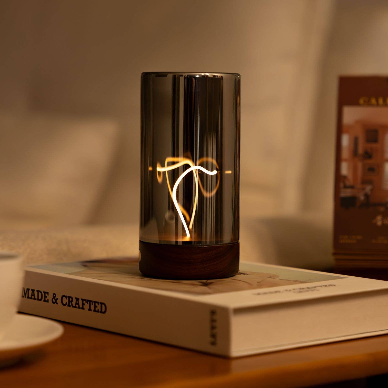 Decorative lamp on a book with a cup and a plant in the background