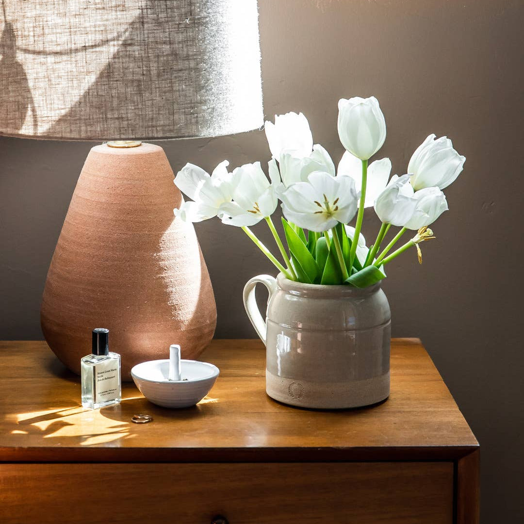 White tulips in a vase on a wooden surface with a lamp and small bowl in the background.