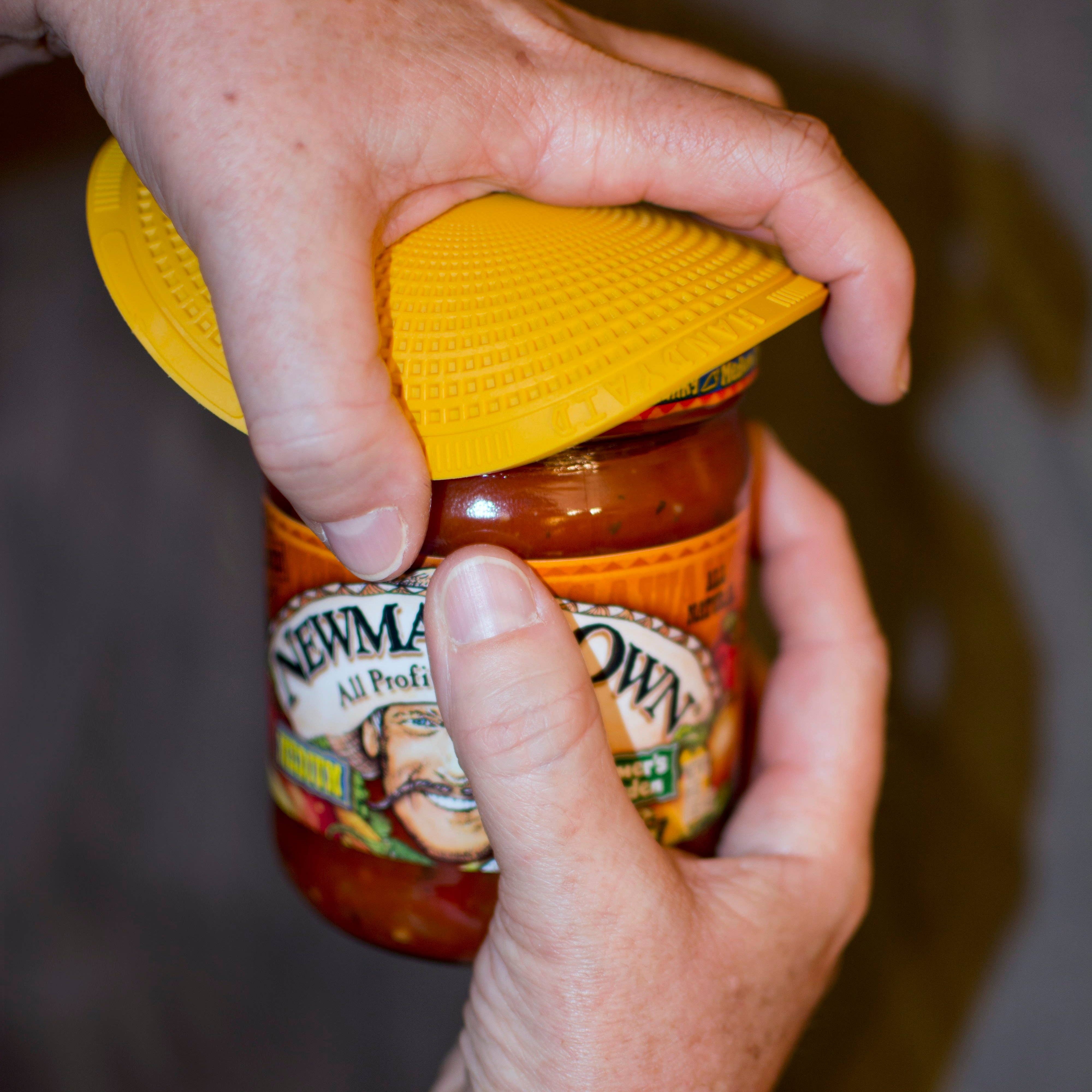 The HANDYAID Jar & Bottle Opener being used on a jar with two hands holding it